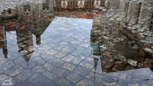 Spiegelung von Burg und Rathausturm in einer Pfütze auf dem Burgplatz